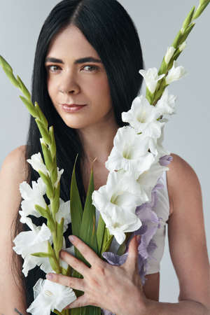 So beautiful. Portrait view of the tender brunette woman posing to the camera with bouquet of gladioli flowers. Female appearance conceptの写真素材