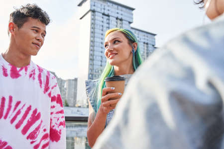 Girl with color air holding cup with coffee and chatting with her friends at the fresh air