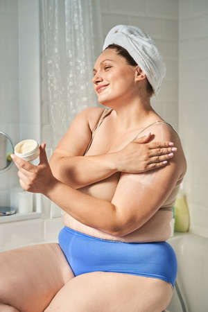 Oversize woman applying cosmetic cream on shoulderの写真素材