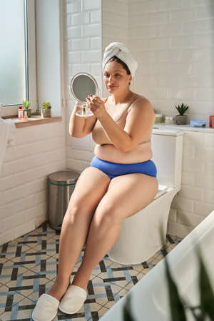 Woman wearing lingerie looking at the mirror while sitting at the bathroomの写真素材