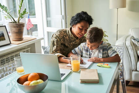 Woman wearing military jacket talking with her little son while sitting at the table with himの写真素材