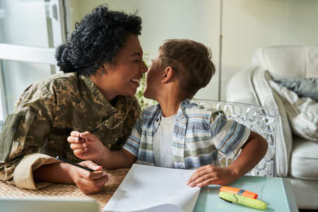 Soldier woman laughing out loud while drawing at the table with her little sonの写真素材