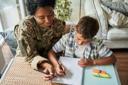 Woman wearing military outfit sitting at the table with her little son and drawingの写真素材