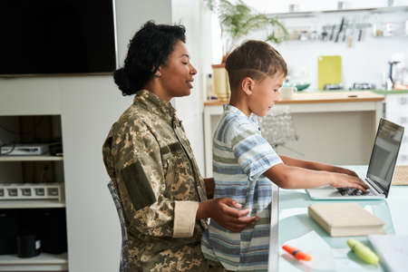 Multiracial little boy sitting at the laps of his mother and typing at the laptop keyboardの写真素材
