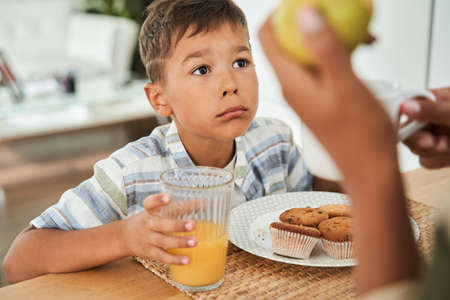 Boy looking at his lovely mother during the breakfast while holding glass of orange juiceの写真素材