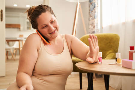 Woman looking at nails and talking on mobile phoneの写真素材