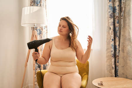 Oversize woman drying wet hair with hairdryer