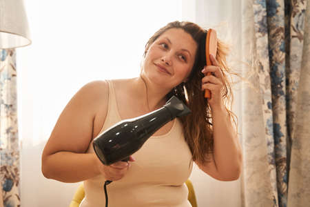 Oversize woman drying wet hair with hairdryerの写真素材