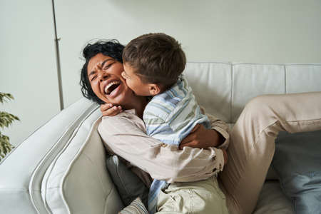 Cute little boy embracing his lovely mother while sitting at the sofaの写真素材