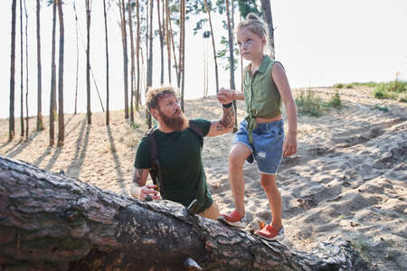 Man helping his daughter walking on fallen tree