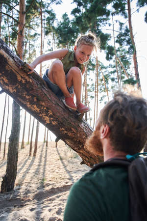 Man looking on girl getting down from fallen treeの写真素材