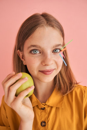 Girl holding apple near her face and smiling to the camera