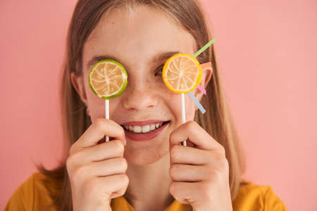 Blonde girl hiding her eyes behind the lollipop, smiling toothy and feeling happyの写真素材