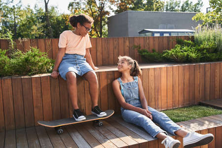 Girlfriends sit on wooden bench with skateboard