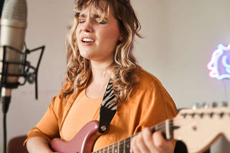 Woman playing guitar and singing in microphoneの写真素材