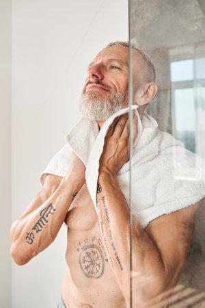 Mature man drying his neck with towel in bathroomの写真素材
