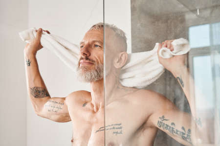 Mature man drying his body with towel in bathroomの写真素材