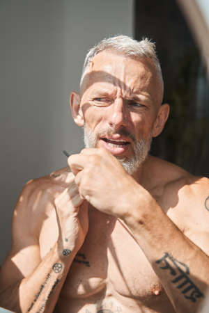 Man standing in the bathroom with naked torso and looking at his reflectionの写真素材