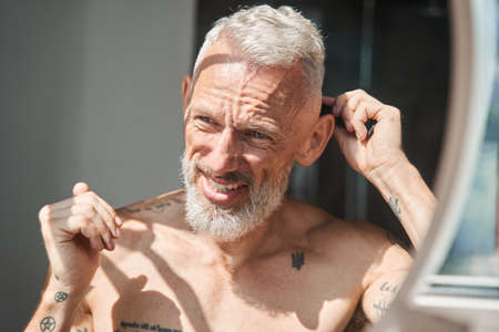 Man standing in the bathroom with naked torso and looking at his reflectionの写真素材