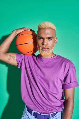 Guy in casual clothes holding ball at his shoulder and looking at the camera