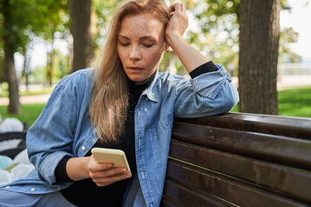 Woman sitting at the bench at the street, looking at the smartphone screen
