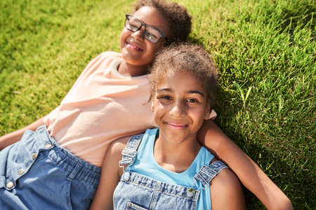 Little black girls lying on grass and huggingの写真素材