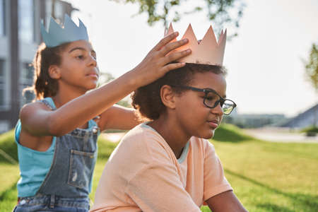 Little girl put paper crown on head of girlfriendの写真素材