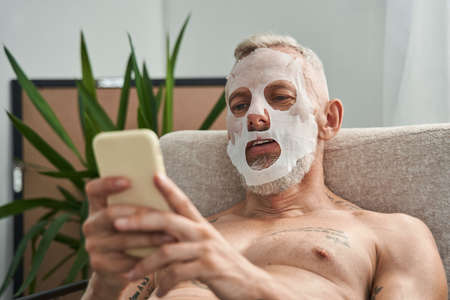 Mature man sit in armchair and use mobile phone