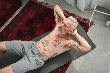 Mature man doing crunching on fitness mat at homeの写真素材