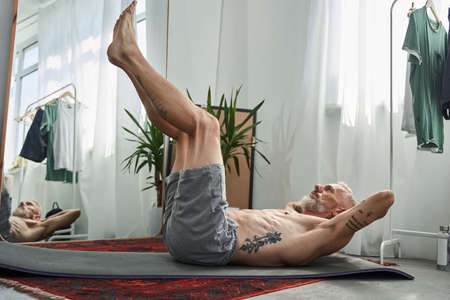 Mature man doing crunching on fitness mat at homeの写真素材