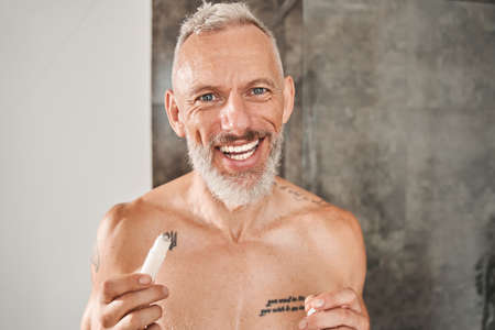 Man laughing out loud and holding moisturizing roller for skin around eyesの写真素材