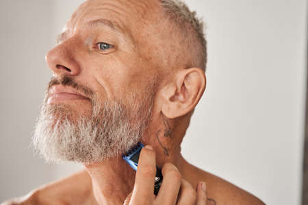 Mature man with naked torso shaving beard with electric razorの写真素材