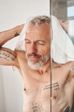 Bearded man wiping his head with white towel at the morningの写真素材