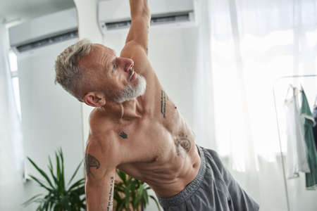 Man with naked torso standing at the mat and doing different exercises at homeの写真素材