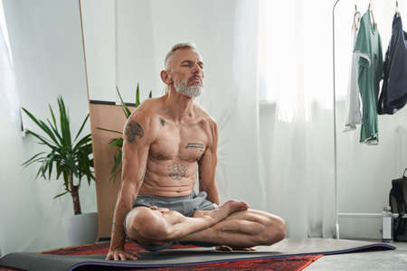 Man sitting cross-legged and holding his body at the hands while enjoying meditationの写真素材