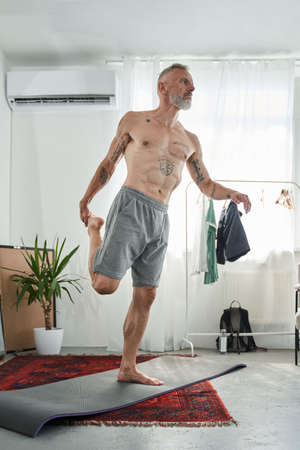 Man with naked torso practicing yoga in warrior pose while standing at the one legの写真素材