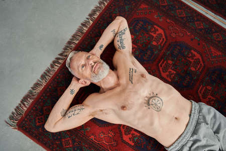 Naked man with tattoos laying at the floor after exercises and relaxingの写真素材