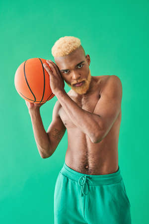 Sportsman with blonde hair playing with orange ball while holding it near his face