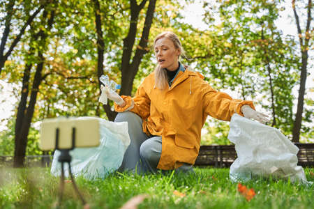 Girl recording her blog at the smartphone during the collecting trash from the parkの写真素材