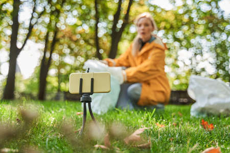 Volunteer woman crouching with bag while picking up trash at the parkの写真素材