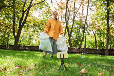 Volunteer woman standing with bag while picking up trash at the parkの写真素材