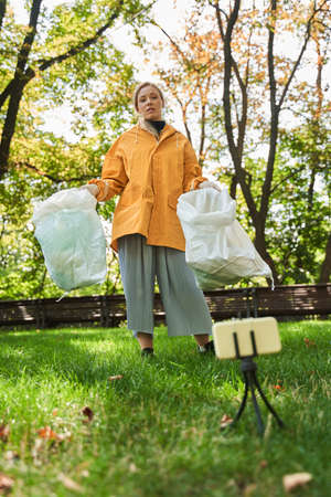 Woman standing in front of the smartphone with rubbish bags and telling about pollutionの写真素材