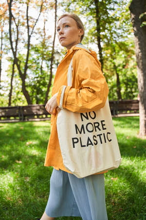 Confident woman with eco bag standing at the park and looking awayの写真素材