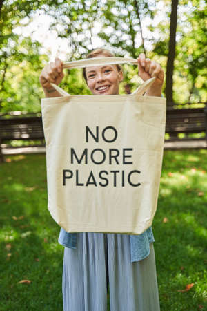 Woman showing to the camera her eco bag with slogan while standing at the parkの写真素材