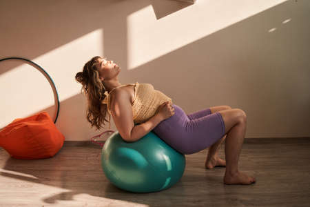 Happy full sized woman exercising at home at the fitness ballの写真素材