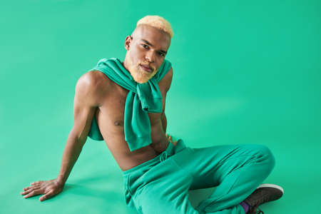 Man in green pants sitting at the floor and looking at the camera with calm expressionの写真素材