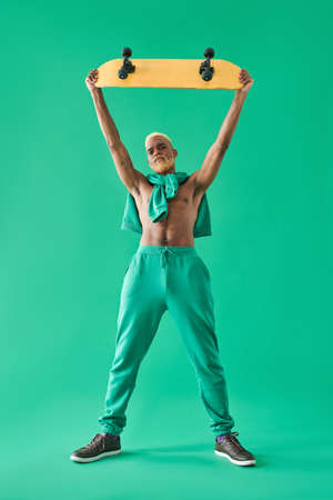 Multiracial boy with naked torso holding his wooden skateboard on outstretched armsの写真素材