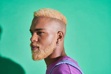 Multiracial man with blonde hair looking away while standing on green backgroundの写真素材
