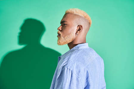 Multiracial gentleman with blonde hair looking away while posing isolated on greenの写真素材