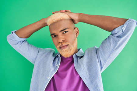 Man with blonde hair looking at the camera while posing isolated on green backgroundの写真素材